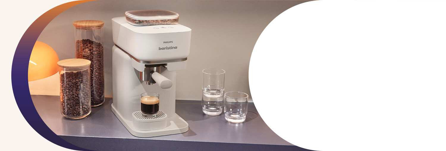 Na blacie stoi ekspres do kawy z filiżanką espresso, obok znajdują się dwa słoje z ziarnami kawy i dwie szklanki. Na ekspresie widnieje napis \'PHILIPS baristina\'.