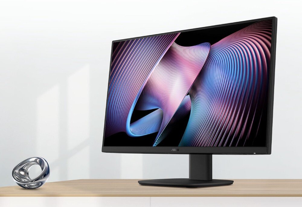 Komputer All in One ASUS VM640KA-BPC019W Monitor All-in-One pod kątem z tapetą w fioletowo-niebieskie fale, obok na drewnianym blacie chromowana ozdoba