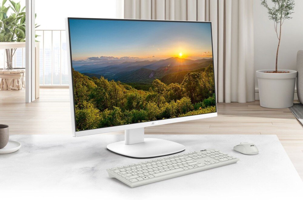 Komputer All in One ASUS VM640KA-BPC019W Komputer All-in-One na biurku z klawiaturą i myszką, na ekranie tapeta z krajobrazem górskim o zachodzie słońca, w tle salon z wyjściem na taras
