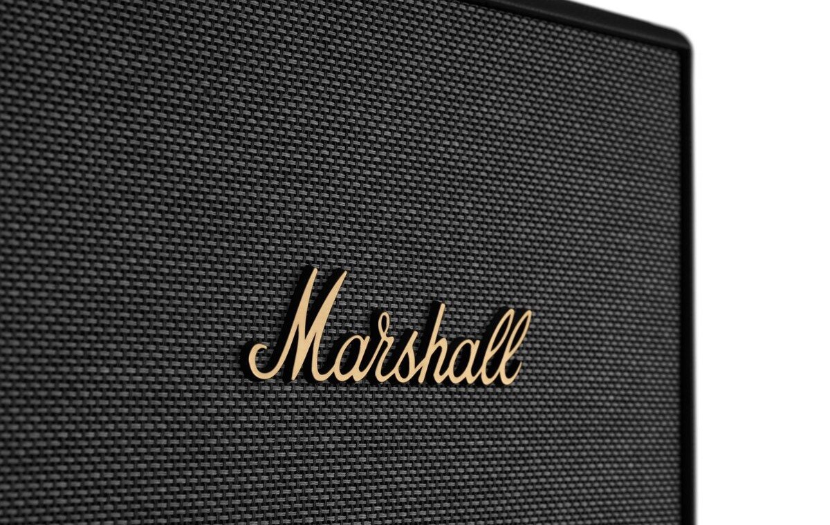 Zbliżenie na czarną kratkę głośnika z widocznym złotym logo \'Marshall\'.