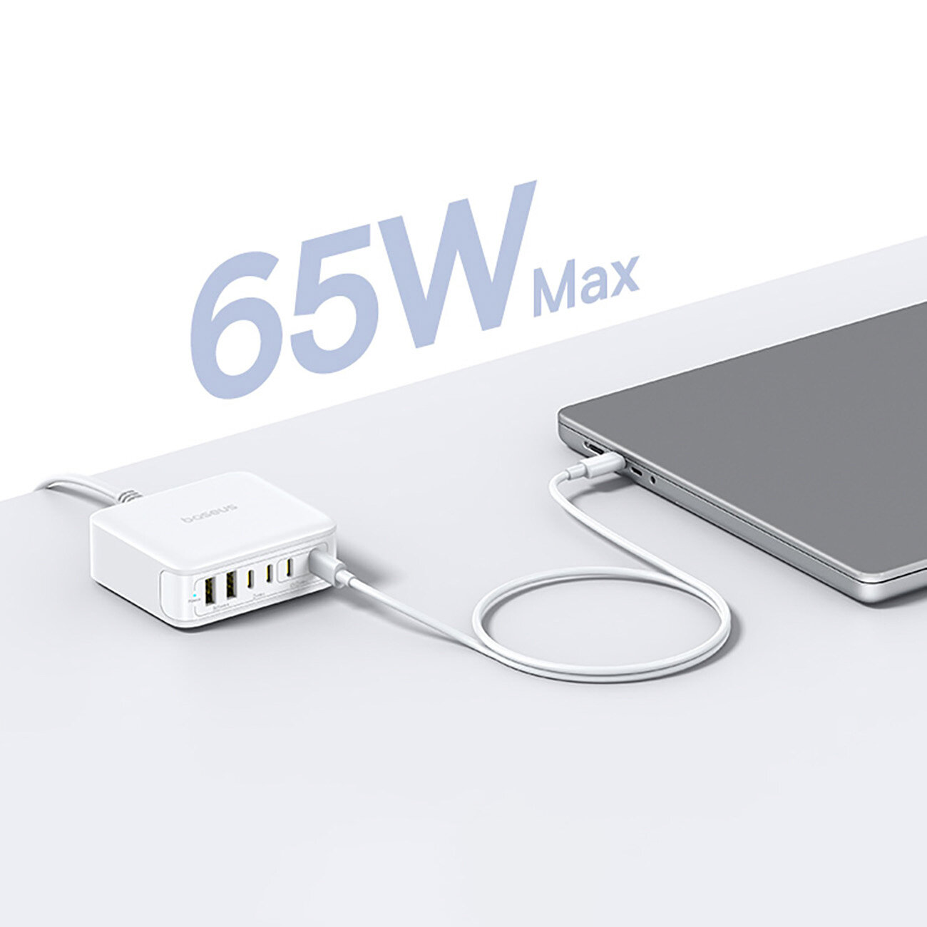 Na białym tle znajduje się biała ładowarka z kilkoma portami USB, podłączona do laptopa. Widoczny jest napis \'65W Max\'.
