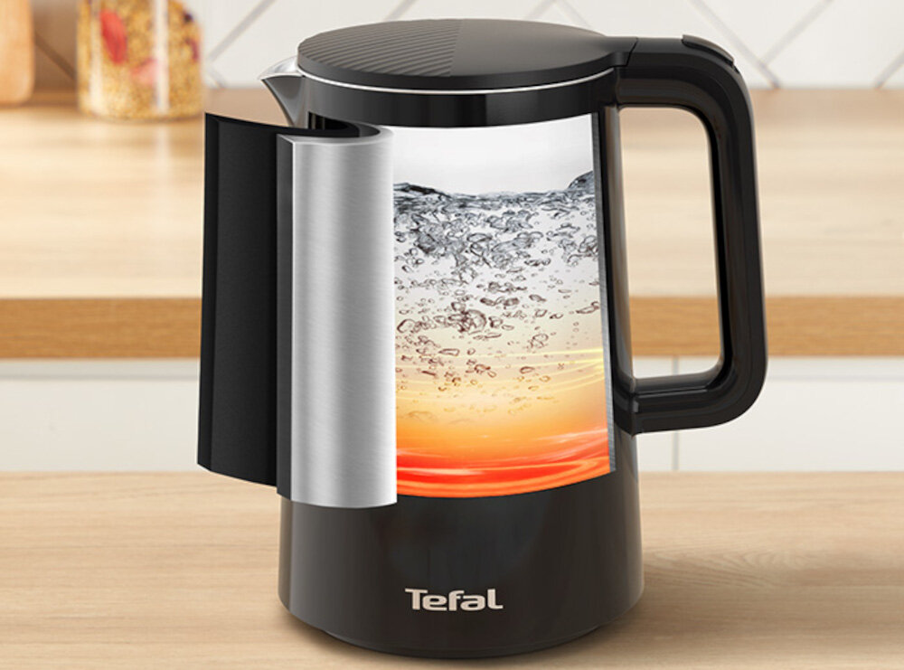 Czarny czajnik z przezroczystą częścią pokazującą gotującą się wodę, z logo \'Tefal\' na dole. Czajnik stoi na blacie kuchennym.