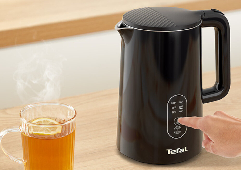 Czarny czajnik z logo Tefal, z panelem dotykowym do regulacji temperatury, obok szklanka z herbatą i cytryną.