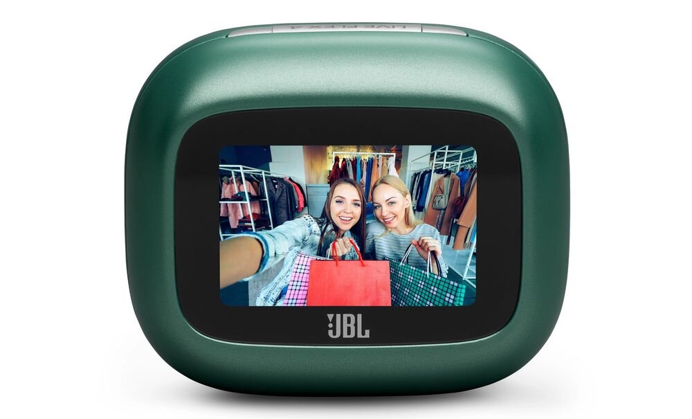Zielone urządzenie z ekranem, na którym widać dwie osoby trzymające kolorowe torby na tle wieszaków z ubraniami. Na obudowie widoczne jest logo \'JBL\'.