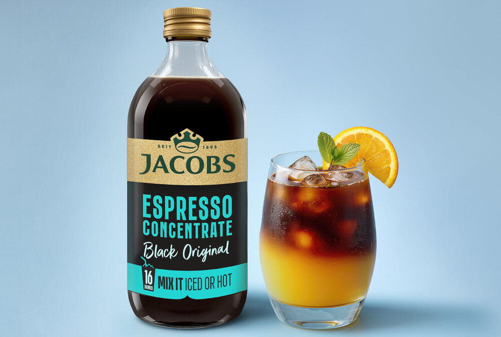 Butelka z etykietą \'JACOBS ESPRESSO CONCENTRATE Black Original\' obok szklanki z napojem, lodem, miętą i plasterkiem pomarańczy na jasnym tle.