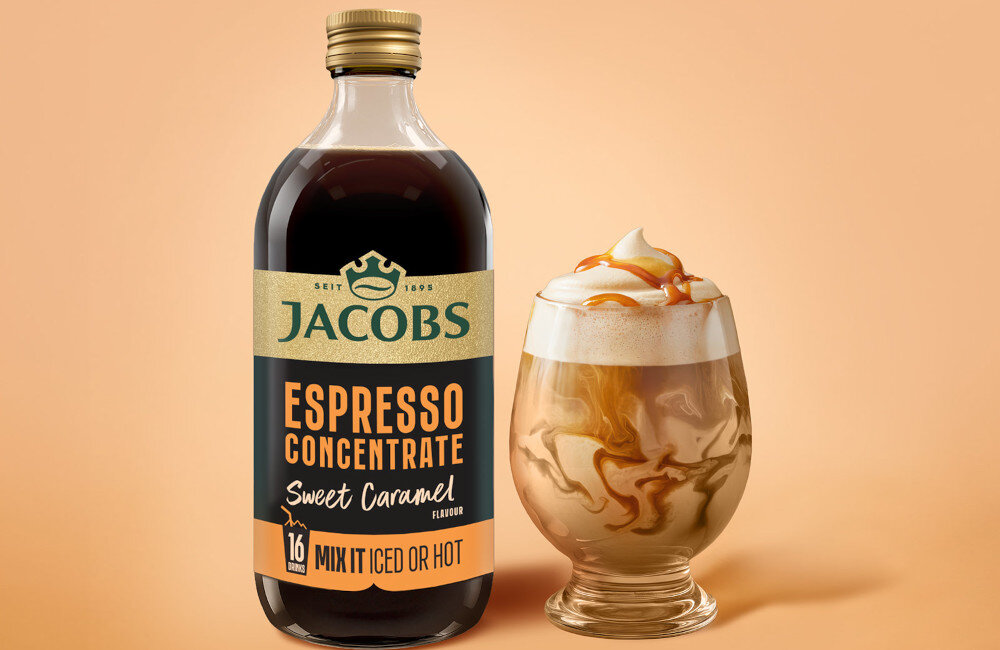 Na obrazie znajduje się butelka z etykietą \'JACOBS ESPRESSO CONCENTRATE Sweet Caramel\' oraz szklanka z napojem o karmelowym kolorze i pianką na wierzchu.