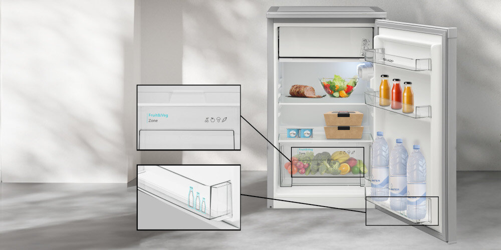 Otwarta lodówka z widocznymi produktami spożywczymi, takimi jak napoje, warzywa i mięso. Na drzwiach lodówki widoczne są napisy \'FrostWay Zone\' oraz logo \'SHARP\'.