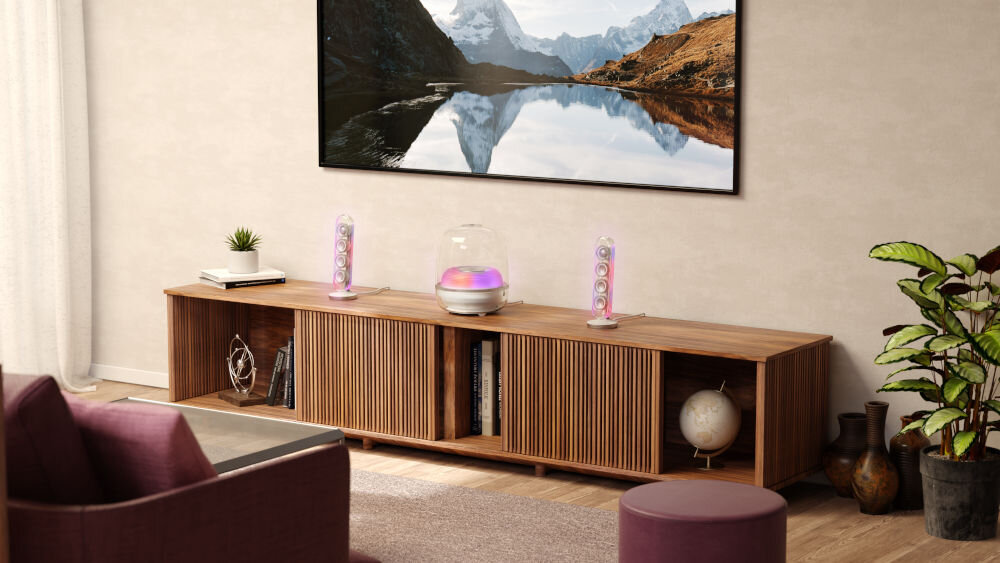 W salonie na drewnianej szafce znajdują się dwa przezroczyste głośniki i centralny subwoofer z podświetleniem. Na ścianie wisi duży obraz przedstawiający górski krajobraz z jeziorem.