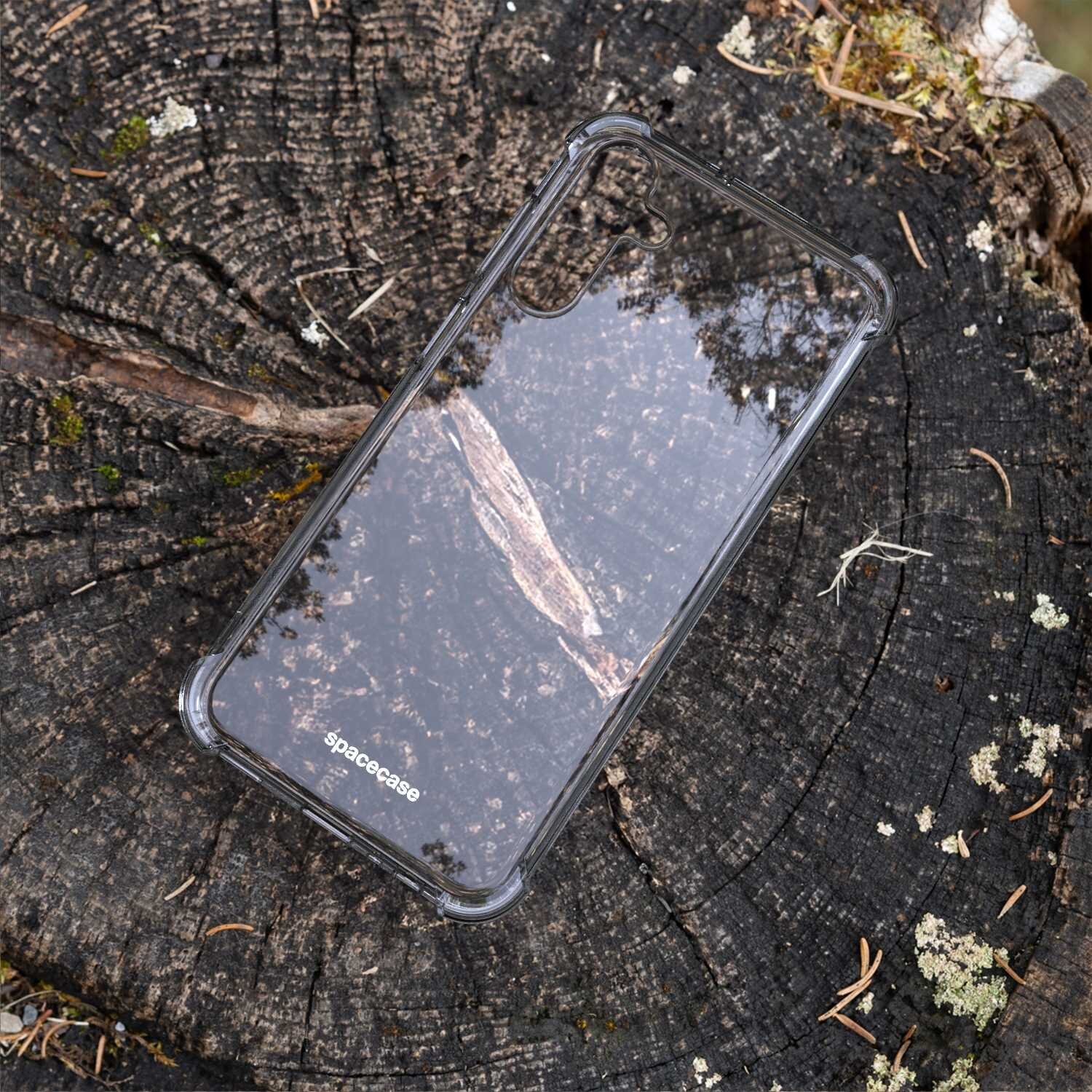 Przezroczyste silikonowe etui na telefon leży na pniu drzewa. Na etui widoczne jest logo \'spacecase\'.