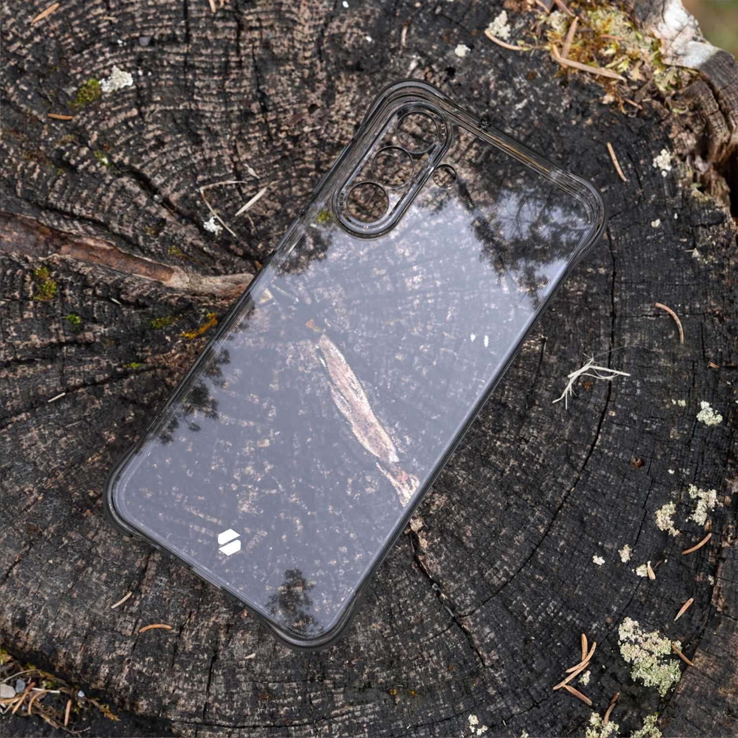 Przezroczyste silikonowe etui na telefon leży na pniu drzewa, ukazując jego strukturę i słoje. Etui ma wycięcia na aparat i przyciski.