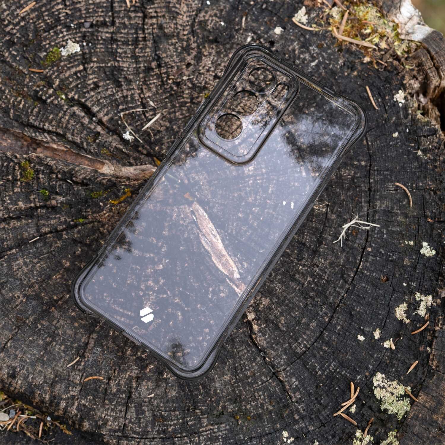 Przezroczyste silikonowe etui na telefon leży na pniu drzewa, ukazując teksturę drewna pod spodem. Na etui widoczne jest małe logo w dolnej części.