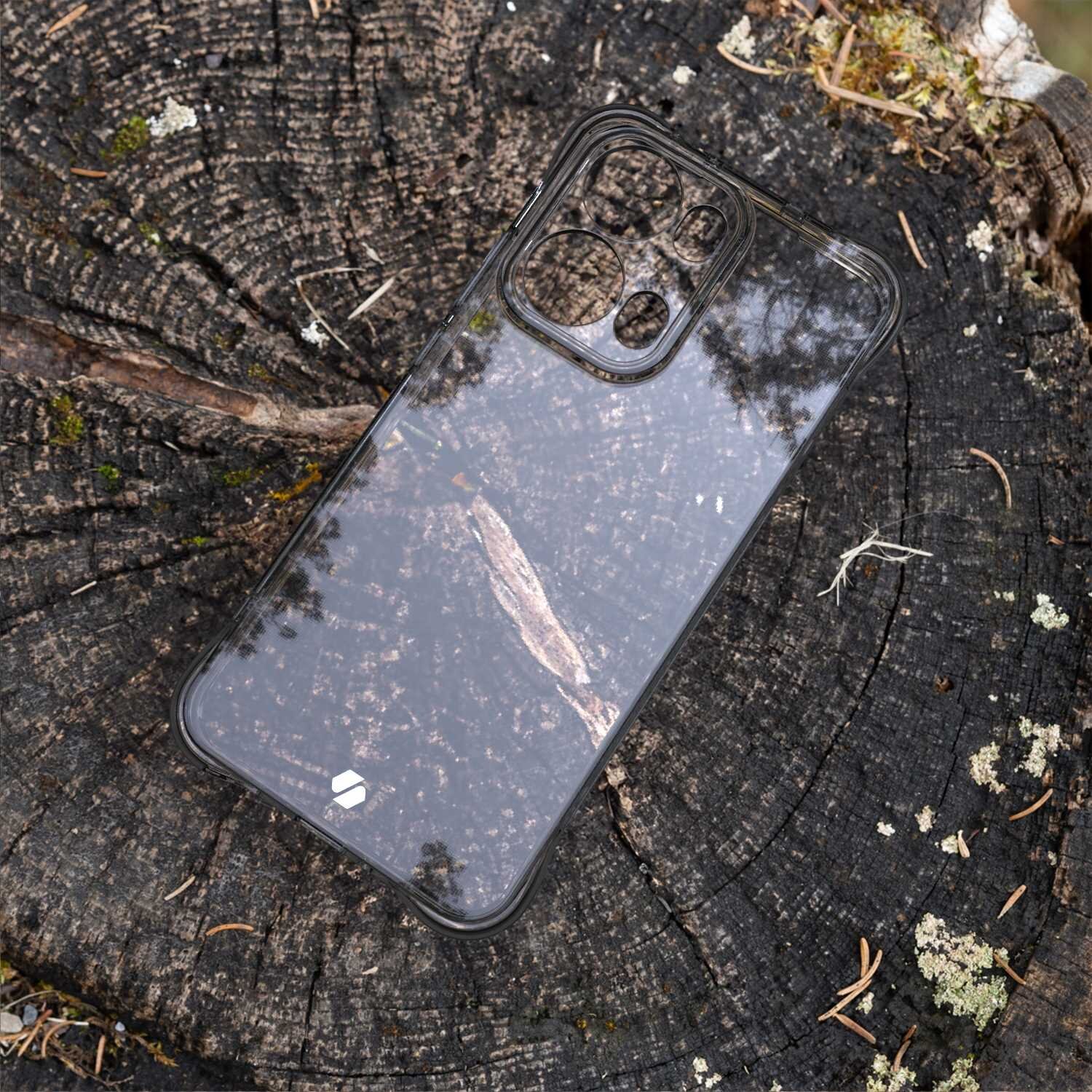 Przezroczyste silikonowe etui na telefon leży na pniu drzewa, ukazując wycięcia na aparat i przyciski. W tle widoczne są tekstury kory i drobne fragmenty mchu.