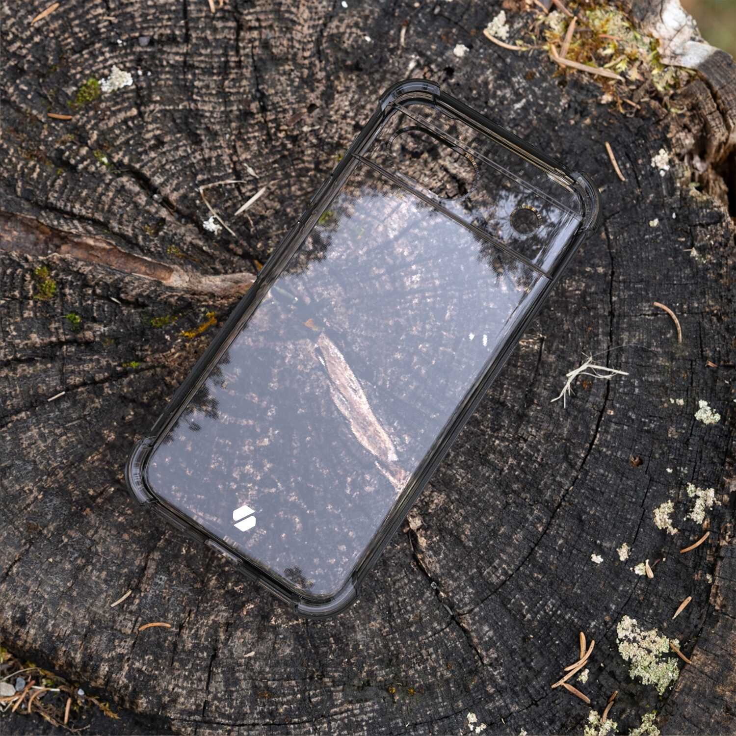Przezroczyste silikonowe etui na telefon leży na pniu drzewa, ukazując jego antywstrząsową konstrukcję. W tle widoczne są tekstury kory i mchu.