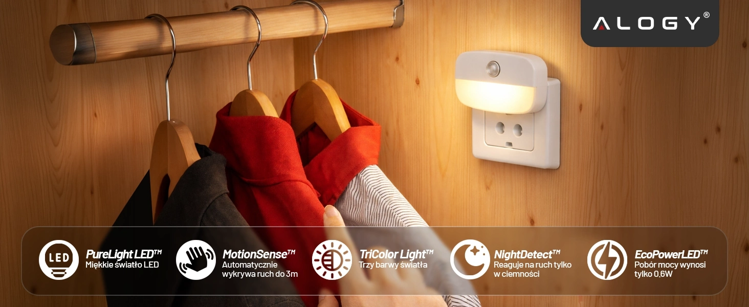Na drewnianej ścianie wisi lampka nocna LED z czujnikiem ruchu, podłączona do gniazdka. Obok znajdują się wieszaki z ubraniami, a na dole widoczne są ikony i teksty opisujące funkcje lampki, takie jak \'PureLight LED\', \'MotionSense\', \'TriColor Light\', \'NightDetect\', \'EcoPowerLED\'.