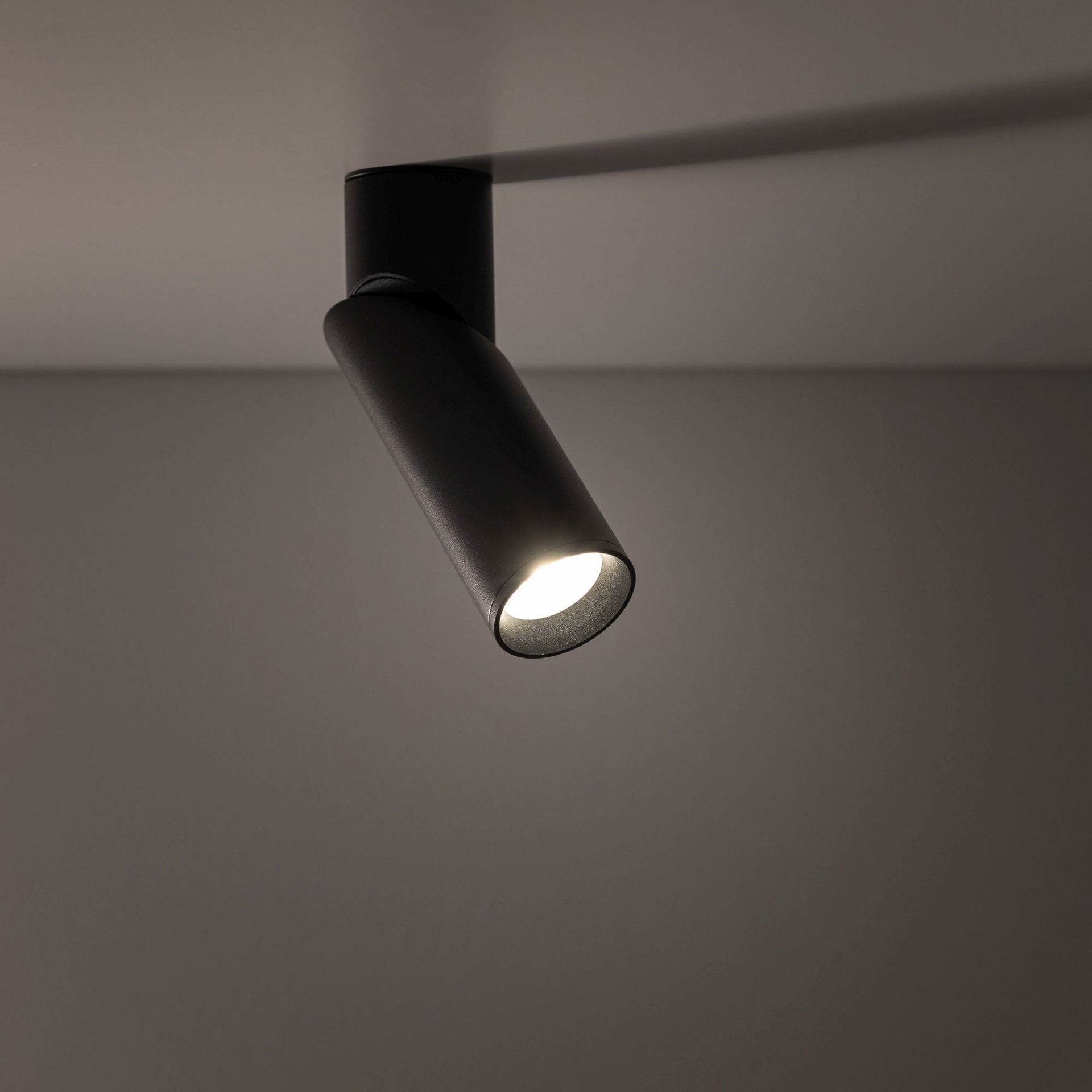 Czarny reflektor sufitowy zamontowany na suficie, emitujący jasne światło. Lampa ma nowoczesny, cylindryczny kształt.