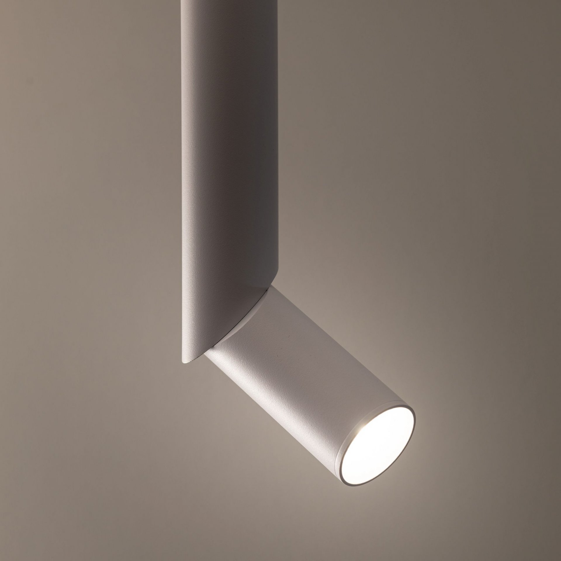 Biała lampa sufitowa z cylindrycznym reflektorem punktowym, emitująca światło na neutralnym tle.