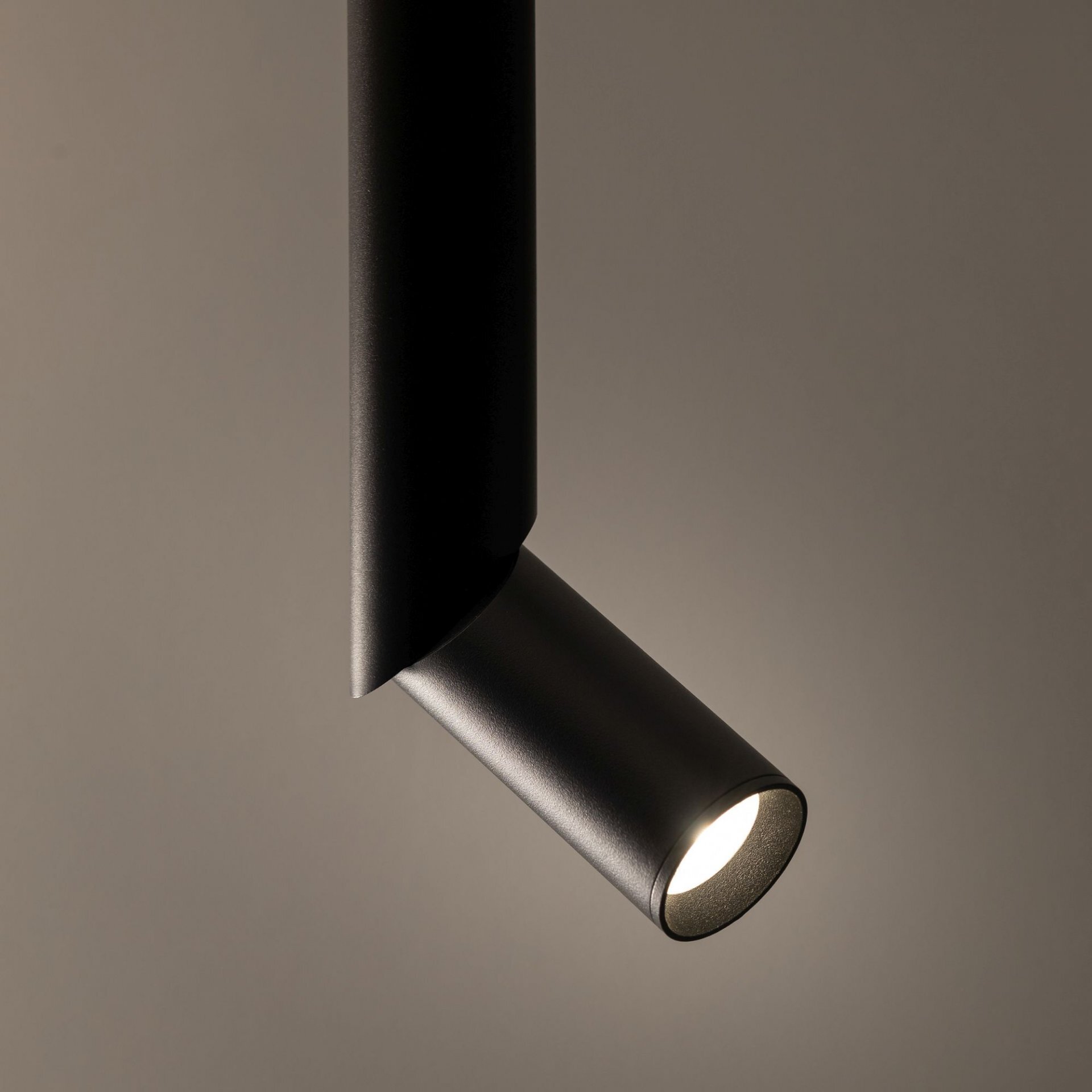 Czarna lampa sufitowa z cylindrycznym reflektorem, emitująca światło w dół. Tło jest jednolite i ciemne.