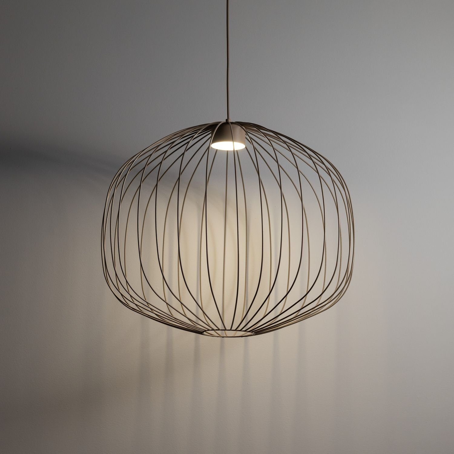 Lampa wisząca o ażurowej konstrukcji z cienkich metalowych prętów, tworzących kulisty kształt. Światło emituje z centralnego punktu, tworząc delikatne cienie na ścianie.