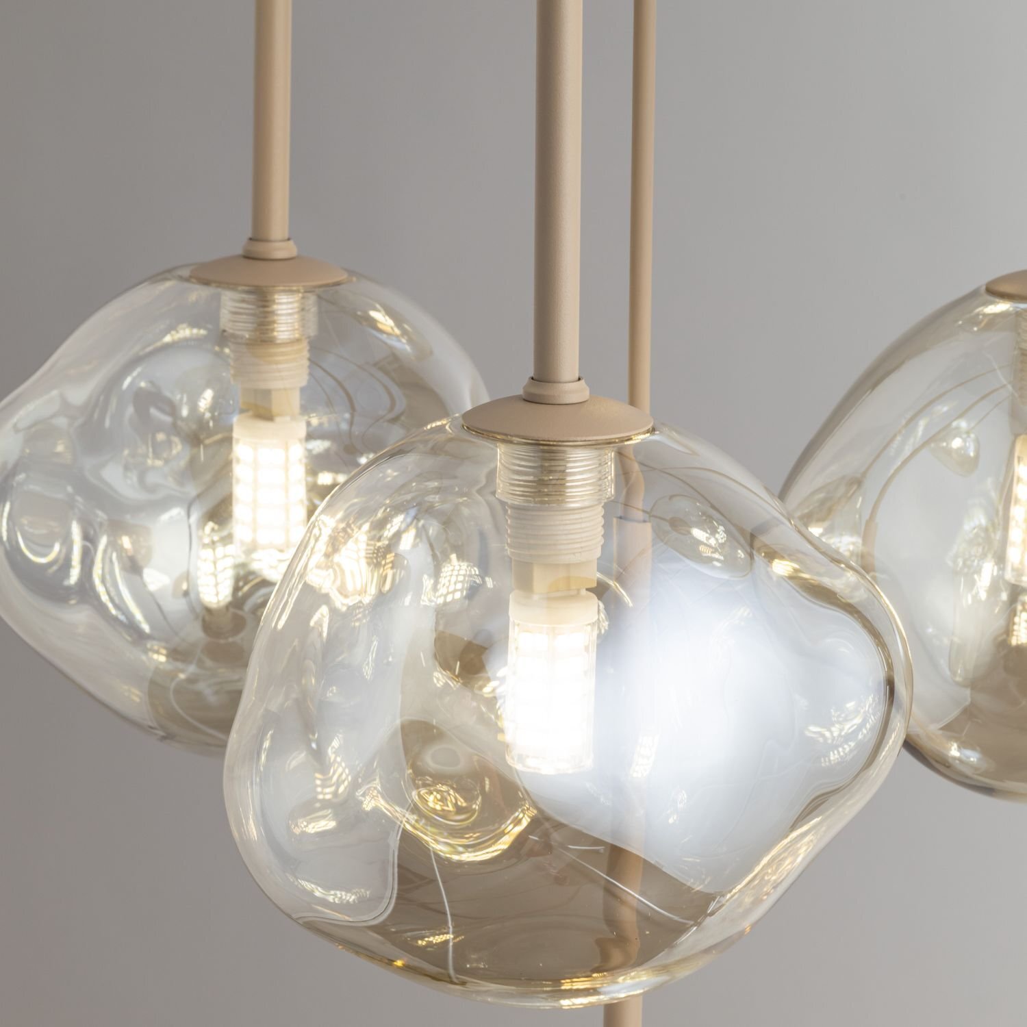 Zdjęcie przedstawia zbliżenie na trzy szklane klosze lamp wiszących z widocznymi żarówkami LED wewnątrz. Klosze mają nieregularny, organiczny kształt i są przezroczyste, co pozwala na widoczność elementów oświetleniowych.