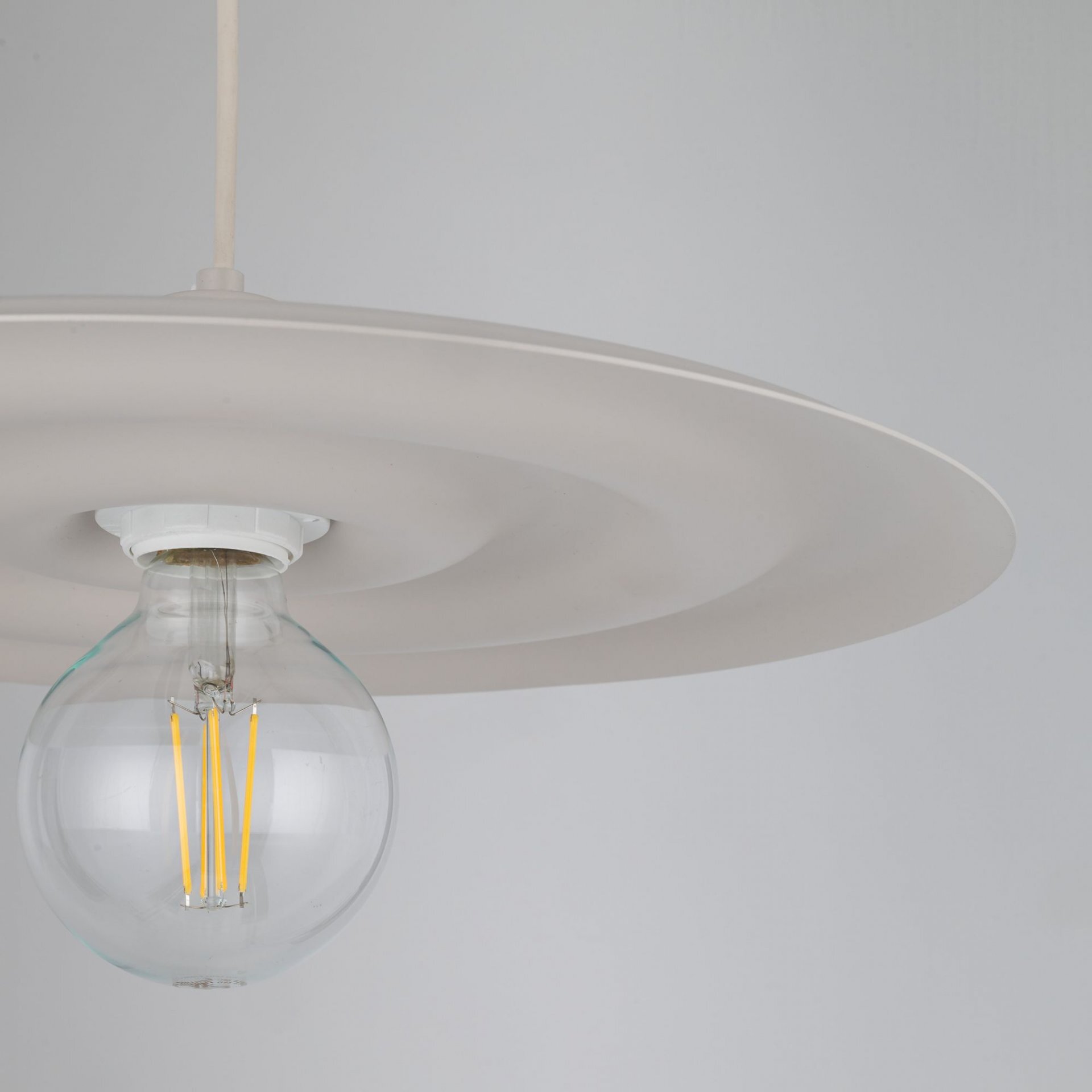Zdjęcie przedstawia lampę wiszącą z dużym, okrągłym kloszem w kolorze kaszmiru i widoczną żarówką z filamentem. Lampa ma nowoczesny design, idealny do salonu lub jadalni.