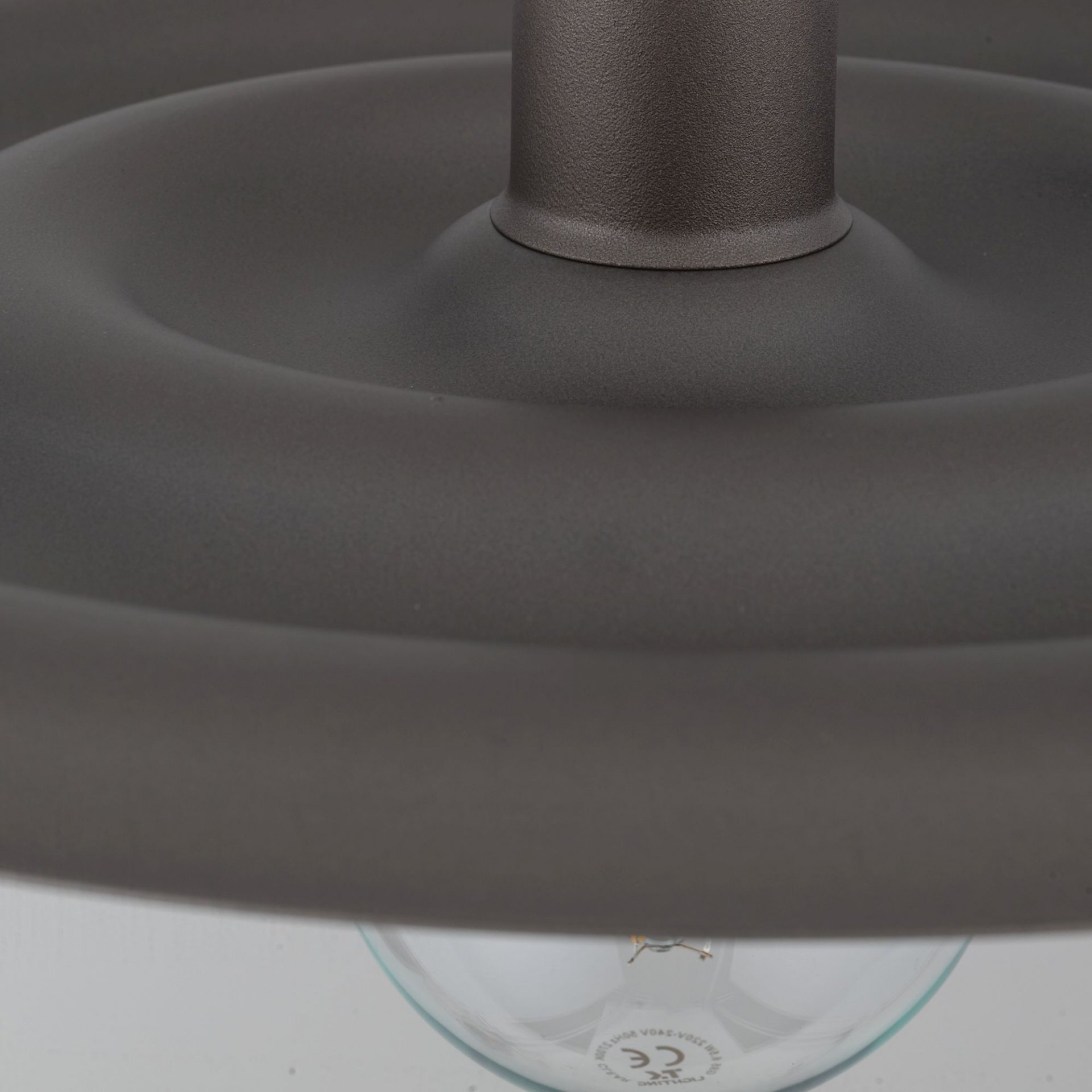 Zbliżenie na brązową lampę wiszącą z widoczną żarówką i metalowym elementem konstrukcyjnym. Na żarówce widoczny jest symbol CE.