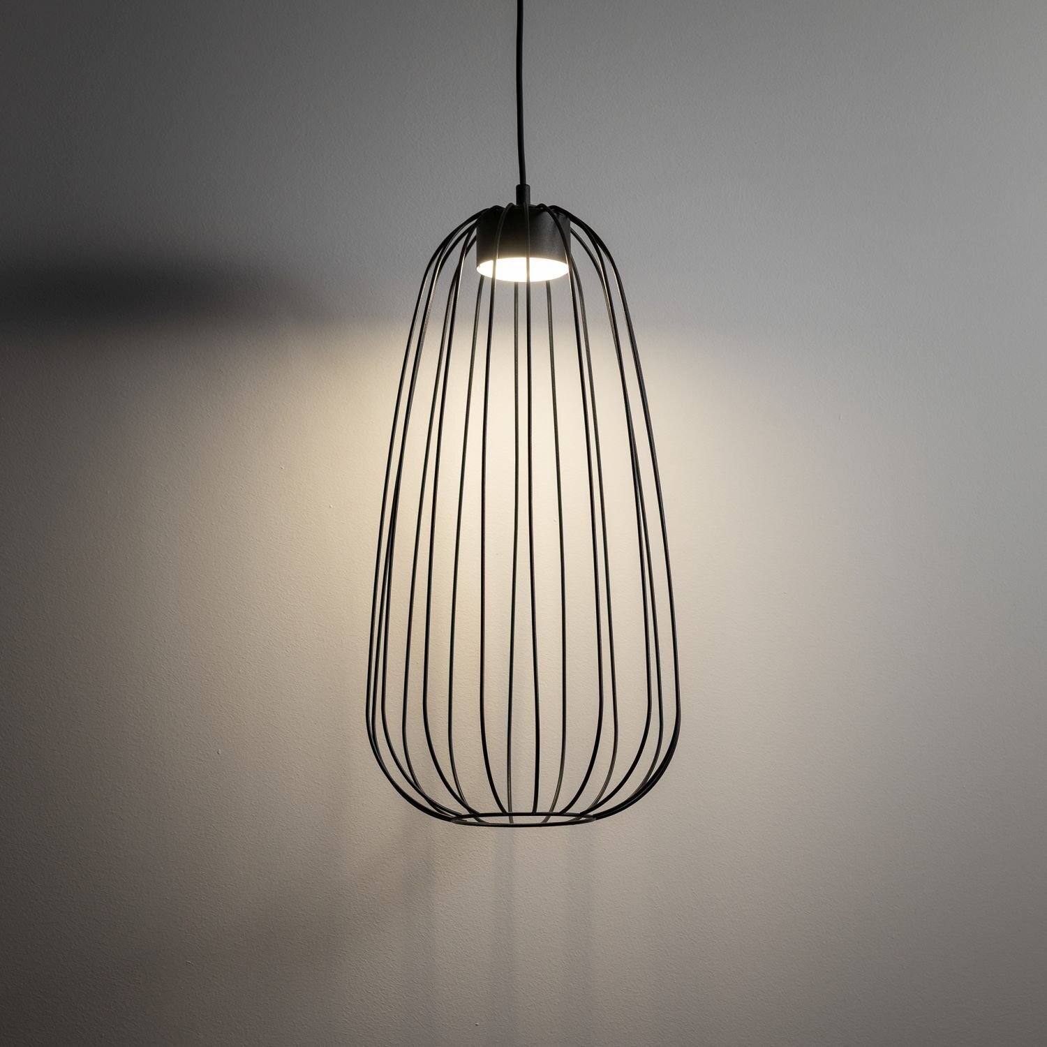Czarna lampa wisząca o nowoczesnym designie z metalowym kloszem w formie klatki, emitująca światło na ścianę. Lampa jest zawieszona na cienkim przewodzie.