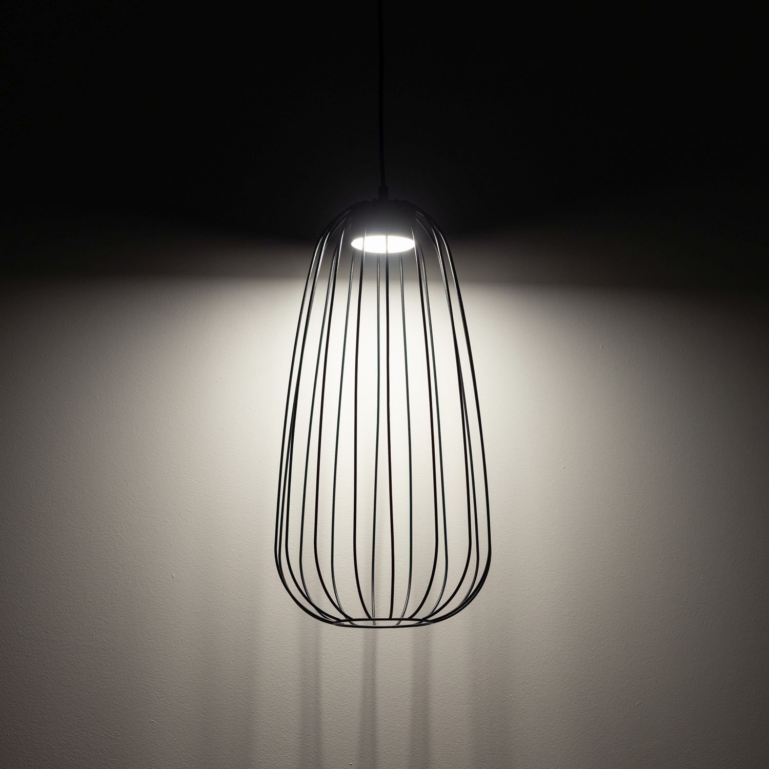 Czarna lampa wisząca o nowoczesnym designie z metalowymi prętami, emitująca światło na ścianę.