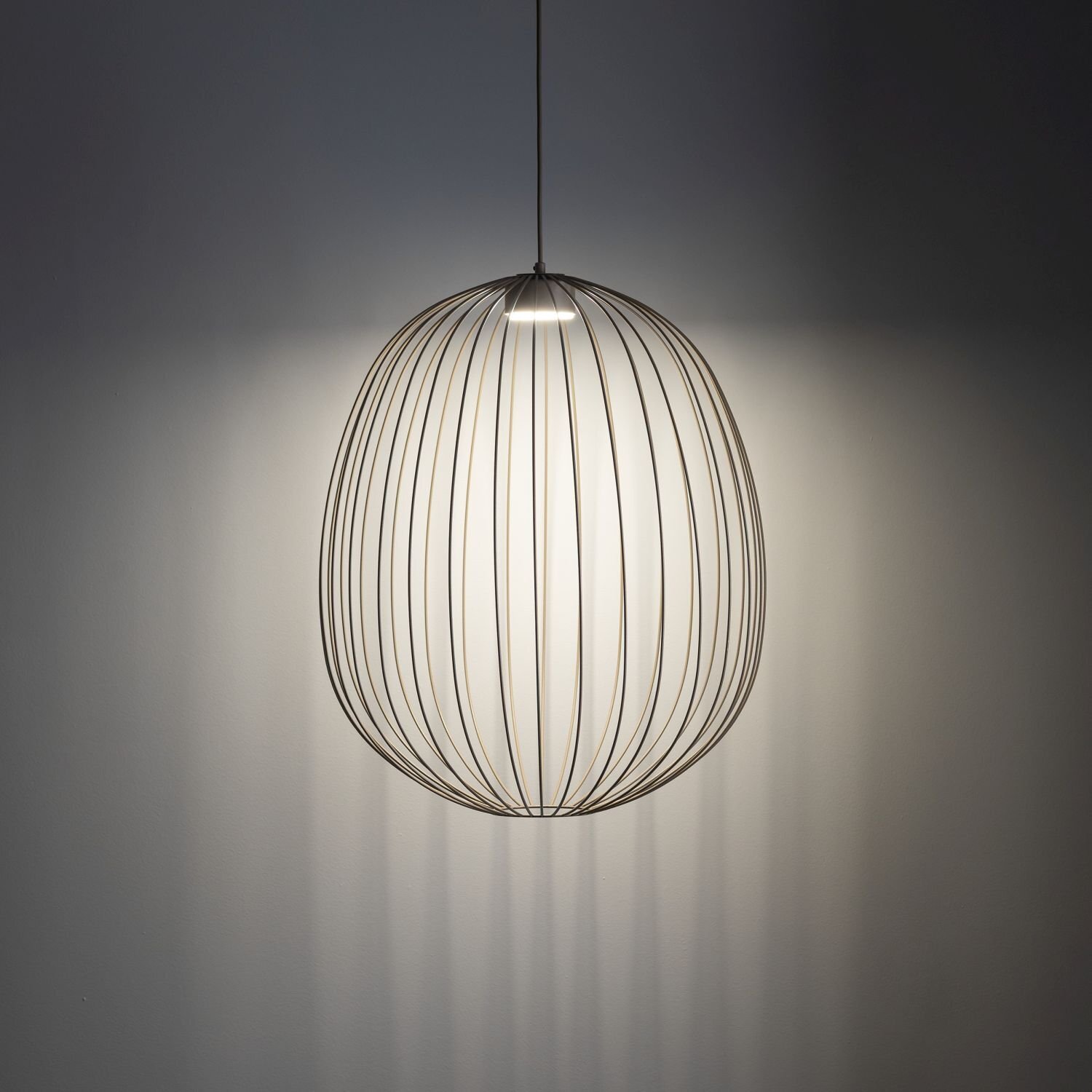 Lampa wisząca o nowoczesnym designie z metalowym kloszem w kształcie elipsy, emitująca światło na ścianę. Klosz składa się z cienkich, równomiernie rozmieszczonych prętów.
