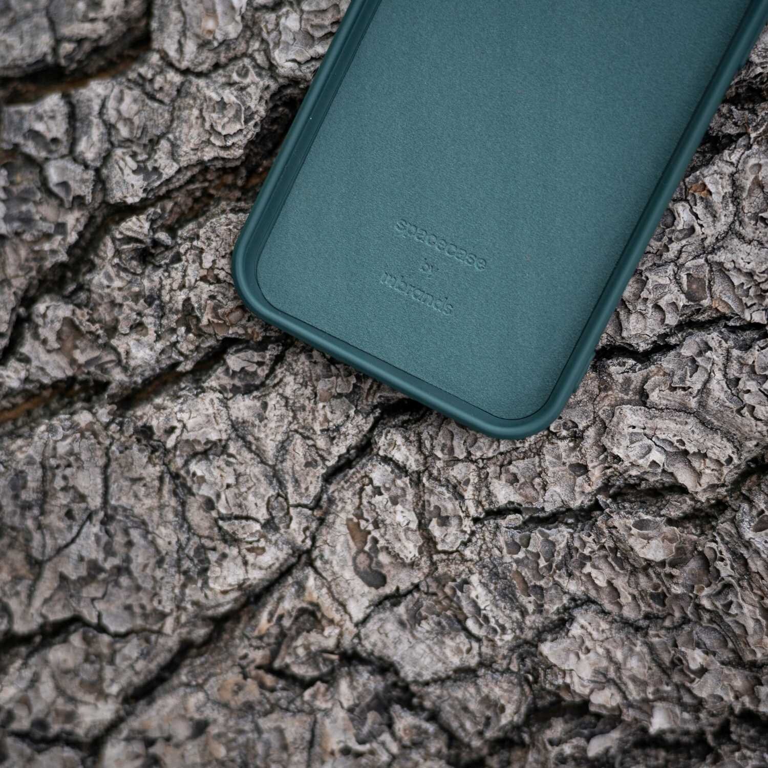 Zielone silikonowe etui leży na powierzchni przypominającej korę drzewa. Na etui widoczny jest tekst: \'spacecase by memumi\'.