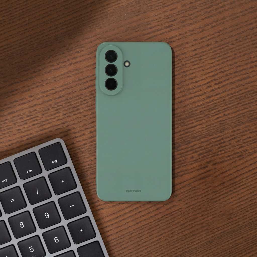 Zielone silikonowe etui na telefon z trzema otworami na aparaty, leży na drewnianym blacie obok klawiatury. Na etui widoczny jest napis \'spacecase\'.