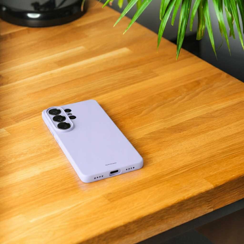 Na drewnianym blacie leży fioletowe silikonowe etui na telefon z trzema dużymi otworami na aparaty. Na etui widoczny jest napis \'SPACECASE\'.