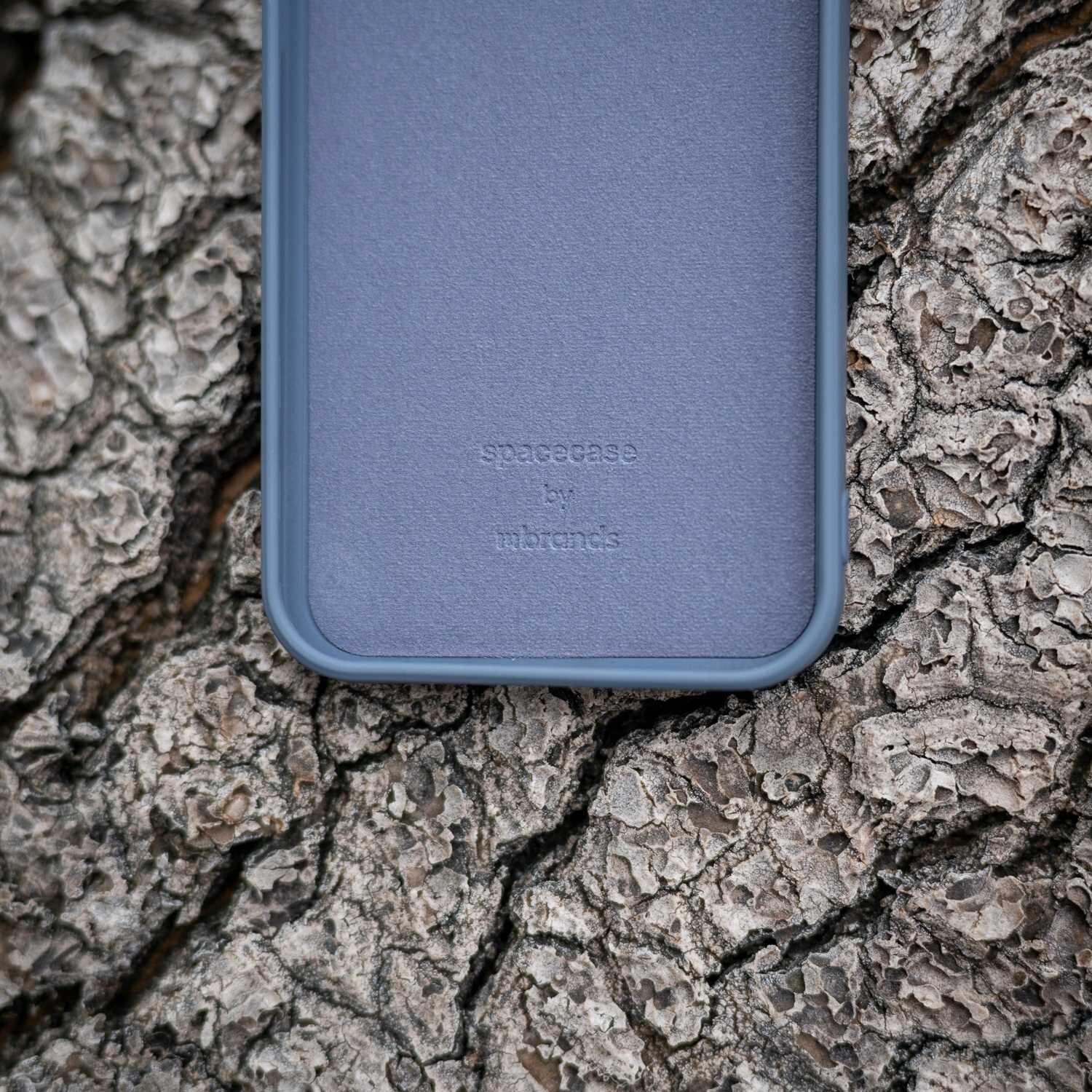 Niebieskie silikonowe etui leży na powierzchni przypominającej korę drzewa. Na etui widoczny jest napis: \'spacecase by mrbrands\'.