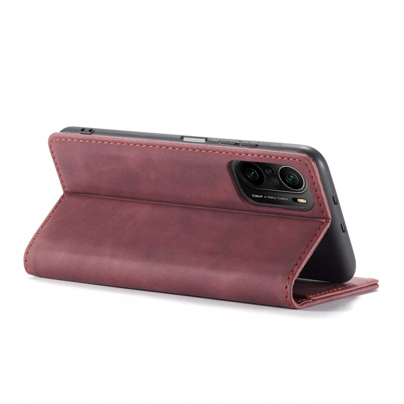 Czerwone etui z klapką ustawione w pozycji stojącej, z widocznymi wycięciami na aparat telefonu. Etui ma gładką powierzchnię i przeszycia na krawędziach.
