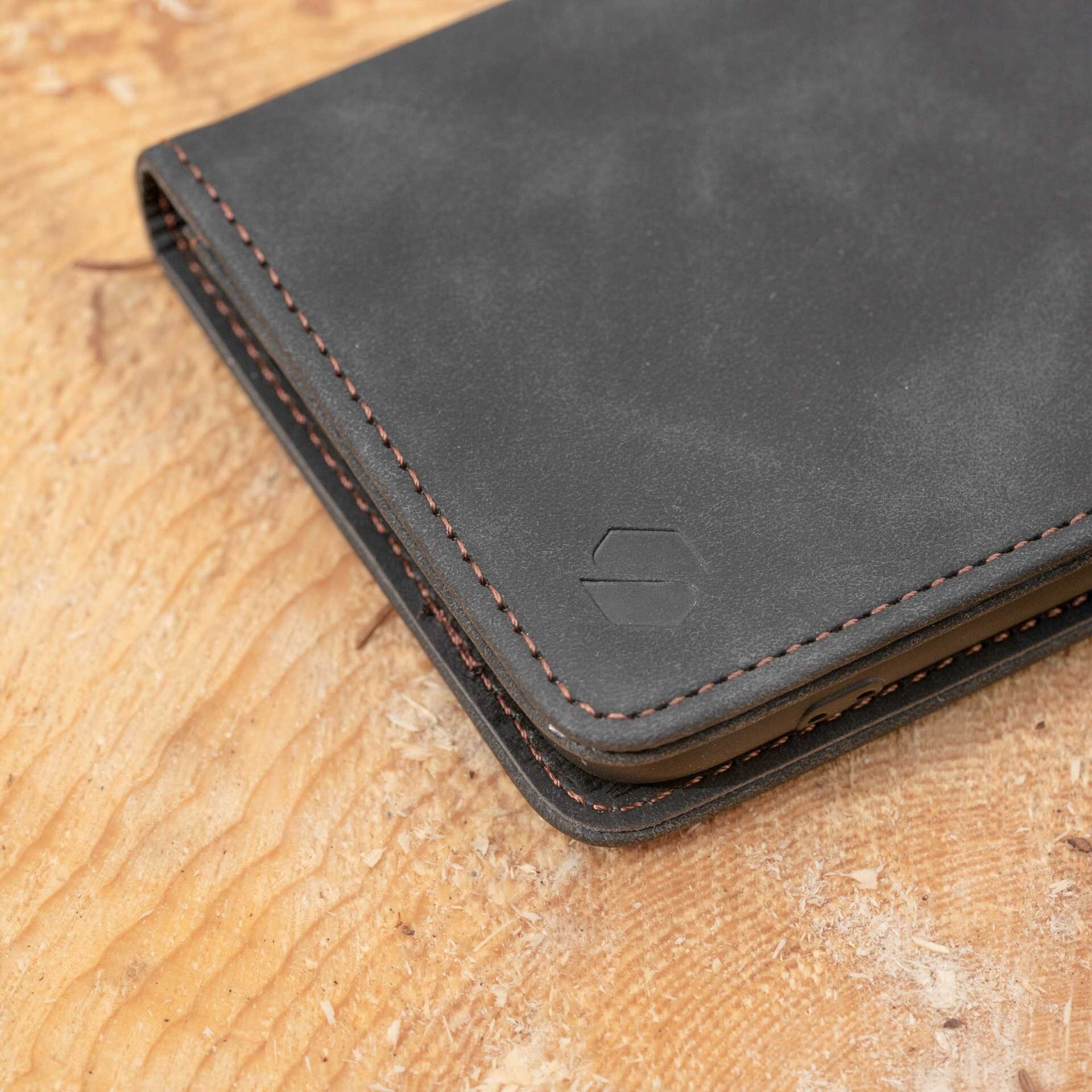 Czarne etui z klapką wykonane z materiału przypominającego skórę, z widocznym logo w kształcie sześciokąta. Etui ma ozdobne przeszycia wzdłuż krawędzi.