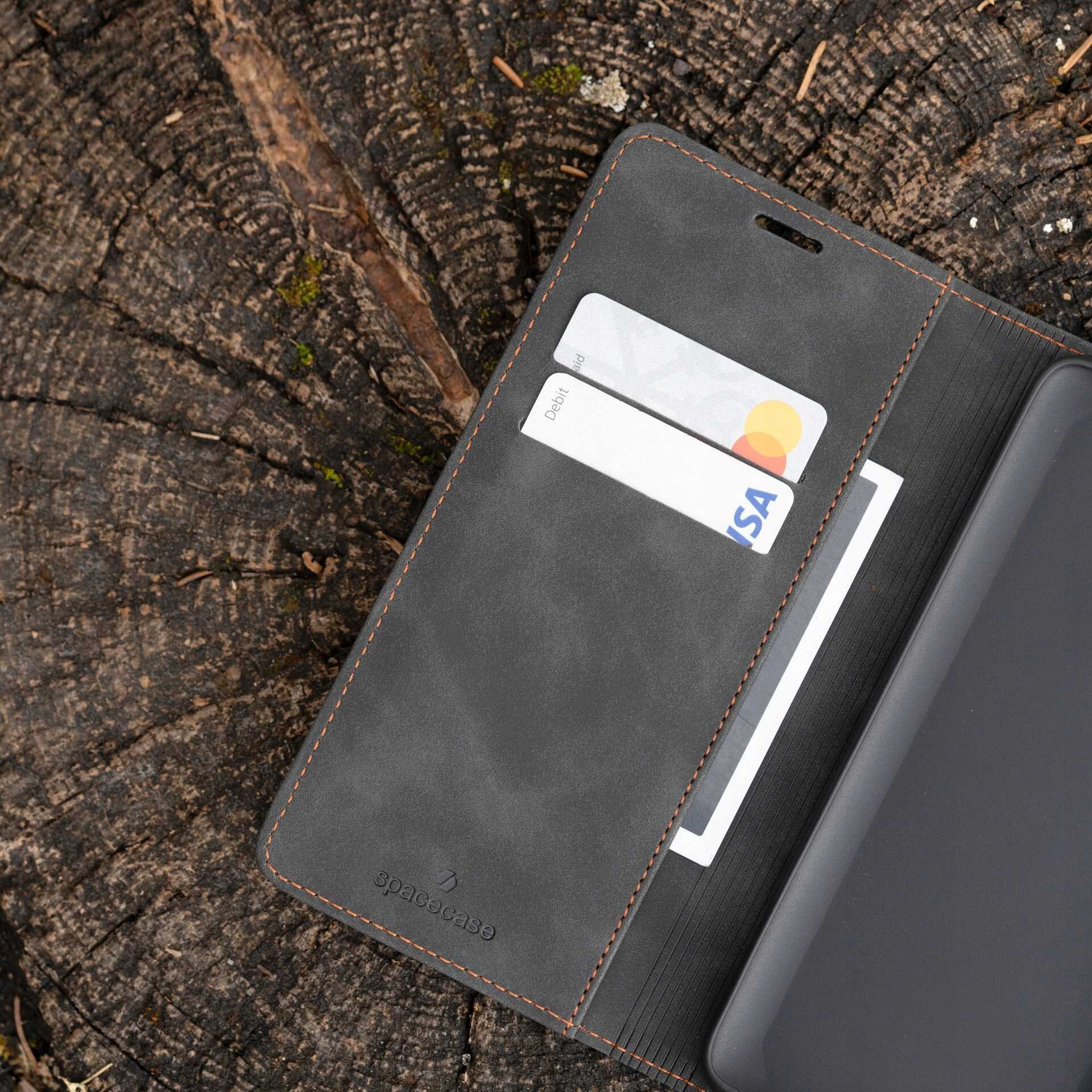 Etui z klapką w kolorze czarnym leży na drewnianym tle, z widocznymi dwoma kartami w kieszeniach. Na etui znajduje się logo \'spacecase\'.