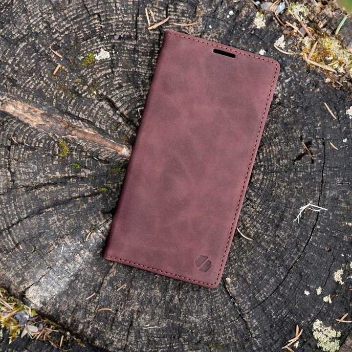 Czerwone etui z klapką leży na pniu drzewa. Na etui widoczne jest subtelne logo producenta.