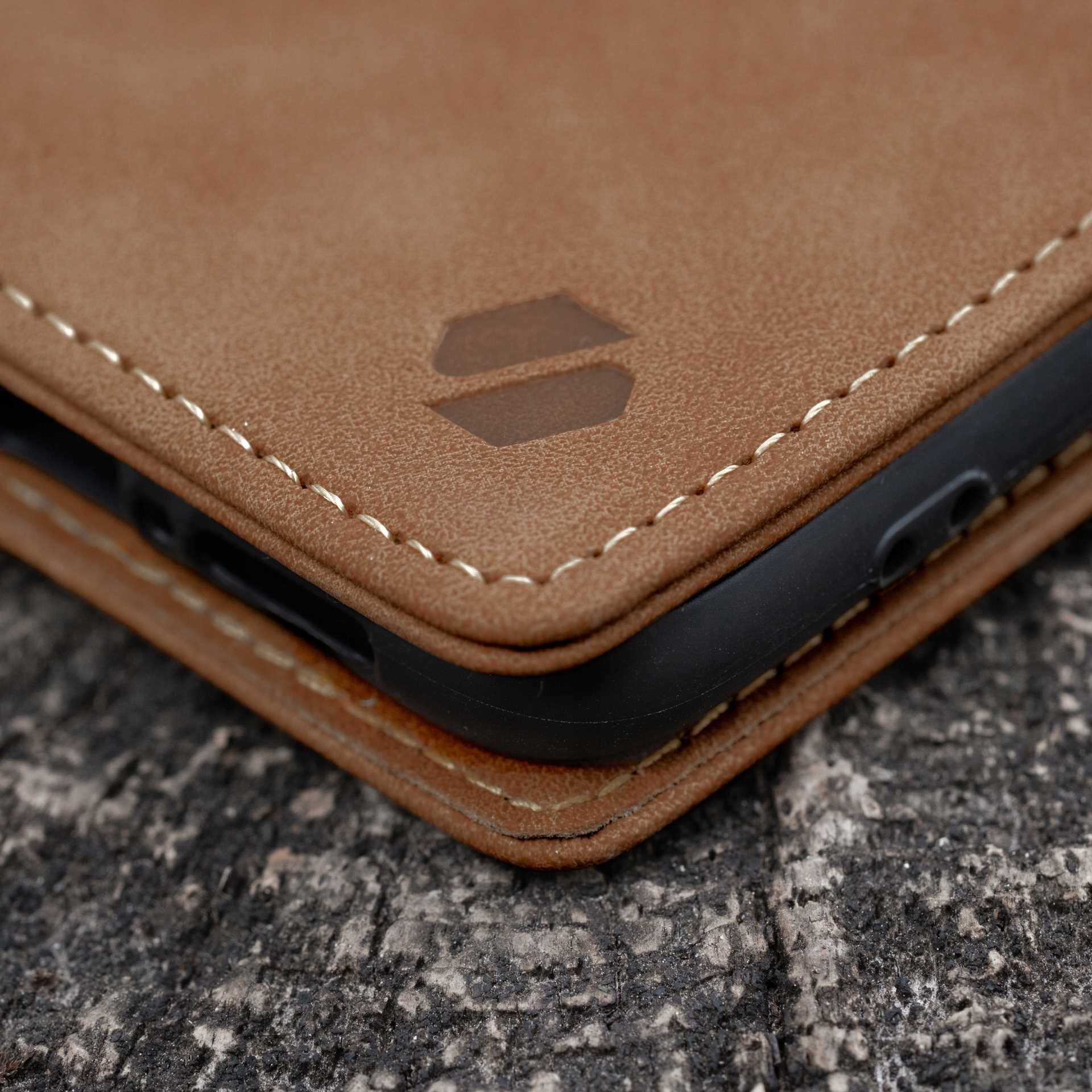Brązowe etui z klapką wykonane z materiału imitującego skórę, z widocznymi przeszyciami i logo w kształcie dwóch sześciokątów. Etui leży na powierzchni przypominającej drewno.