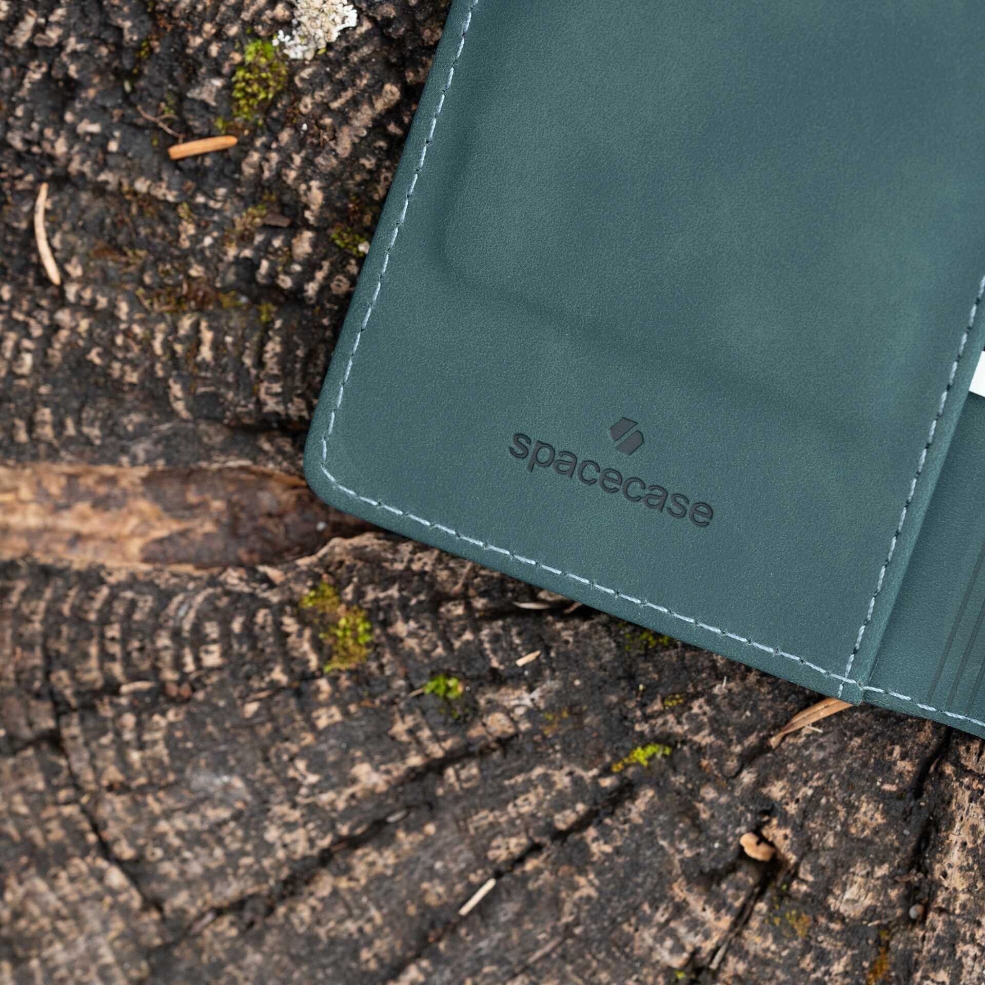 Etui z klapką w kolorze niebieskim leży na drewnianej powierzchni. Widoczne jest logo \'spacecase\' na etui.