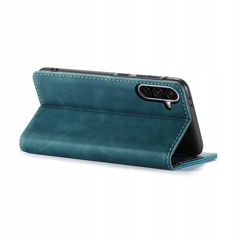 Niebieskie etui z klapką ustawione w pozycji stojącej, z widocznymi trzema otworami na aparat telefonu. Etui ma wyraźne przeszycia na krawędziach.