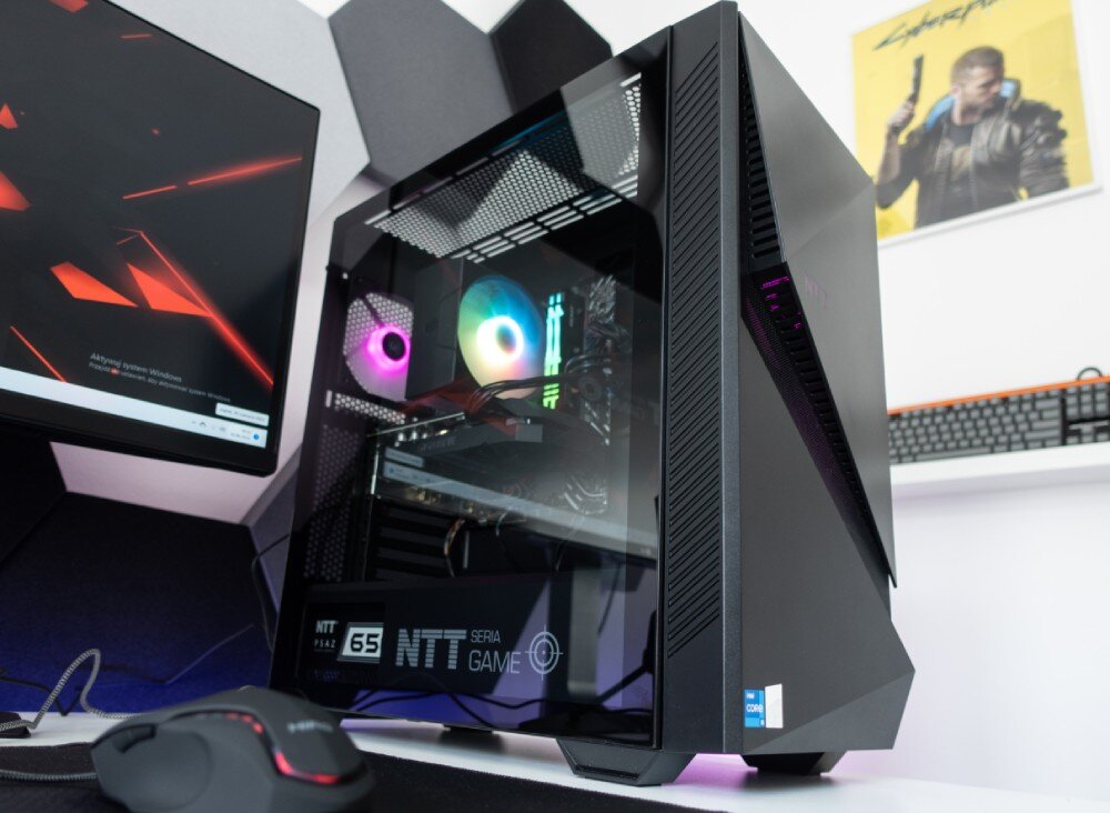 Komputer NTT Game Pro ZKG-I5145060-N01H Obudowa komputerowa z przeszklonym panelem bocznym, przez który widać podświetlone komponenty wewnętrzne, obok stoi monitor