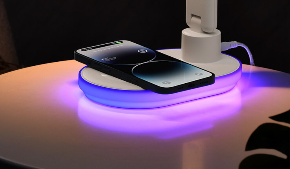 Na zdjęciu widać smartfon leżący na podstawce z fioletowym podświetleniem, która jest częścią lampki biurkowej. Lampka jest podłączona kablem USB.