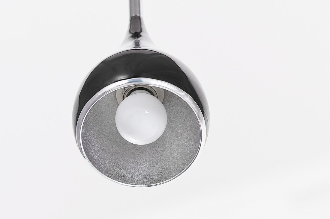 Zdjęcie przedstawia zbliżenie na metaliczną lampę wiszącą z widoczną żarówką wewnątrz. Lampa ma błyszczące, srebrne wykończenie z czarnym akcentem na zewnętrznej części klosza.