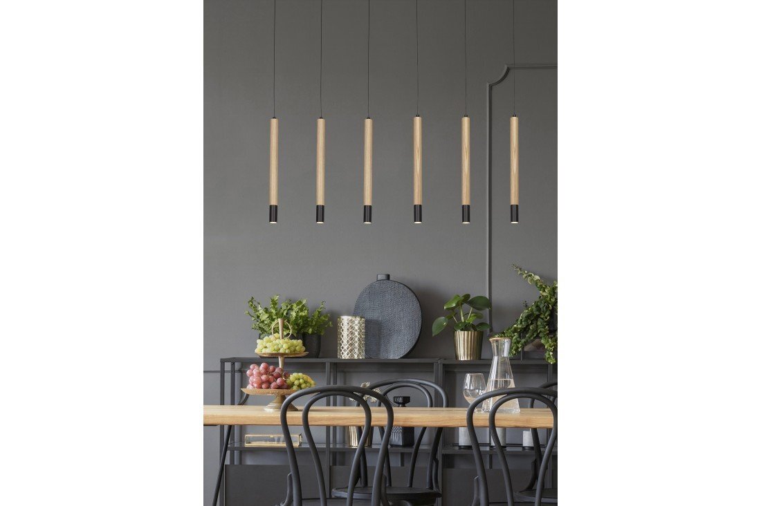 Na obrazie widoczne jest sześć wiszących lamp o nowoczesnym designie, umieszczonych nad stołem z krzesłami. W tle znajduje się półka z dekoracjami i roślinami.
