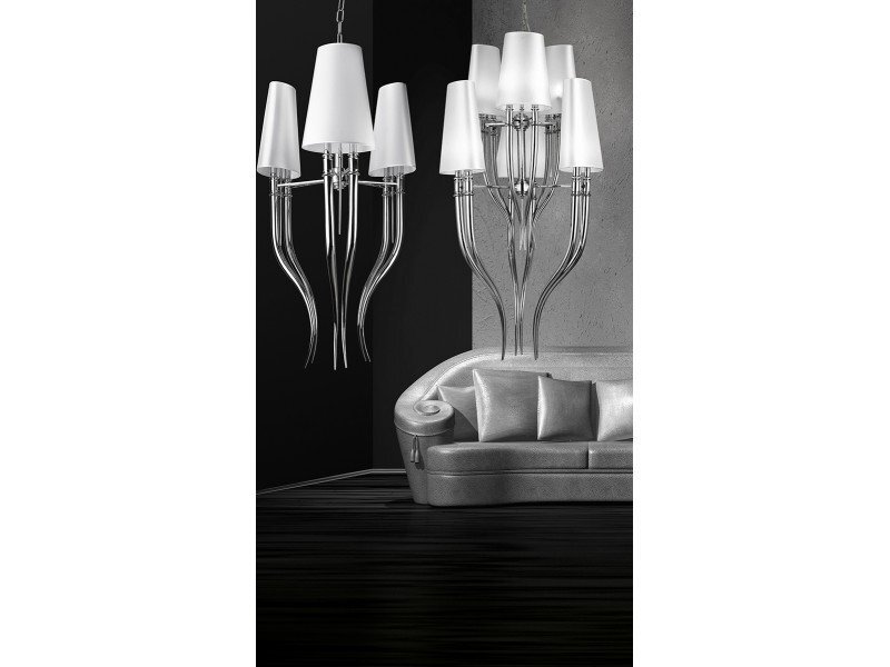 Na obrazie widoczna jest elegancka lampa wisząca z sześcioma białymi kloszami i metalowymi elementami, zawieszona nad srebrną sofą. Tło jest ciemne, co podkreśla nowoczesny design oświetlenia.