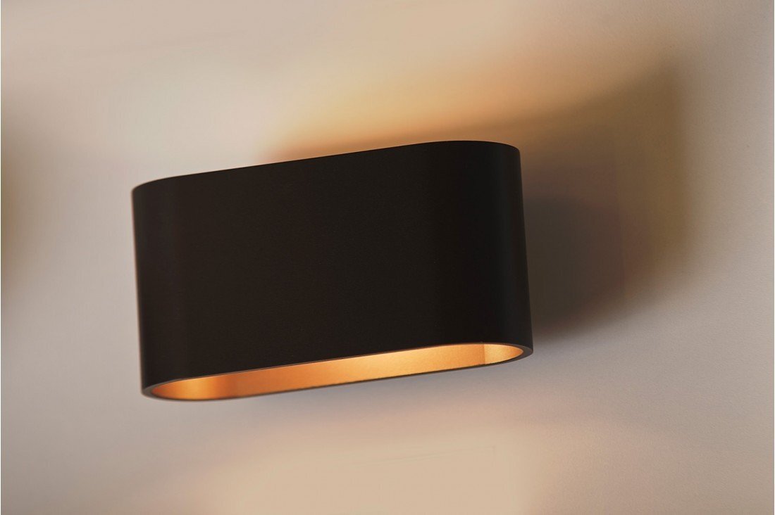 Czarna, prostokątna lampa ścienna z zaokrąglonymi krawędziami, emitująca ciepłe światło od spodu. Lampa zamontowana jest na jasnej ścianie.