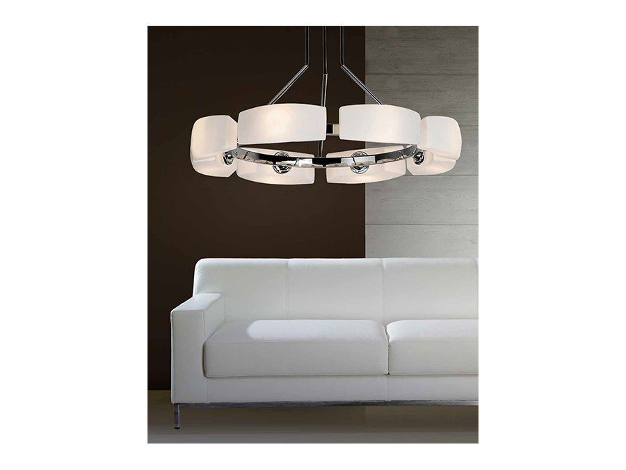 Na obrazie widoczna jest elegancka lampa wisząca z ośmioma białymi kloszami, zawieszona nad białą sofą na tle ciemnej ściany.
