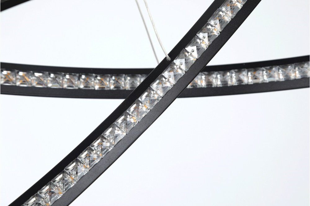 Zbliżenie na elementy lampy wiszącej LED z czarnymi ramami i przezroczystymi kryształkami. Lampa zawieszona jest na cienkich przewodach.