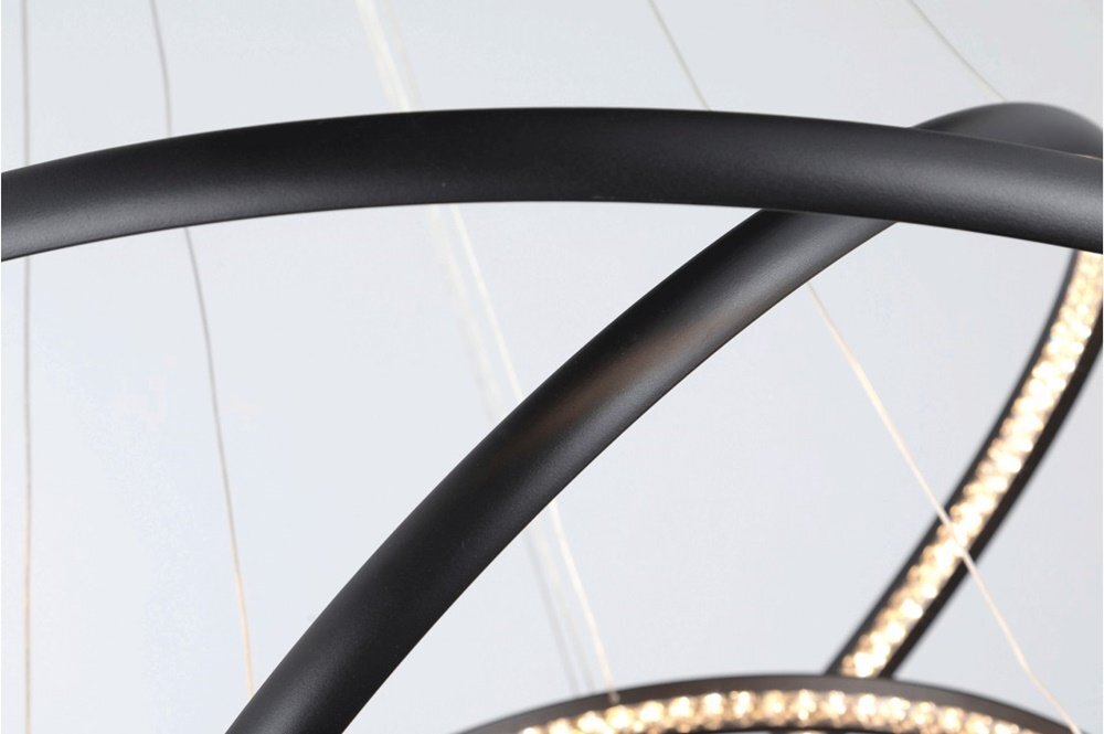 Zbliżenie na czarne, zakrzywione elementy lampy wiszącej z widocznymi diodami LED. Tło jest jasne, a lampa ma nowoczesny design.