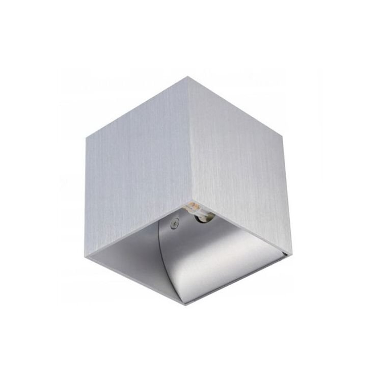 Srebrna, kwadratowa lampa ścienna o nowoczesnym designie, wykonana z metalu. Wnętrze lampy jest również metaliczne, z widocznym miejscem na żarówkę.