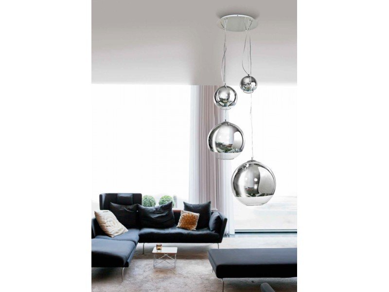 Nowoczesna srebrna lampa sufitowa z czterema kulistymi kloszami wisi nad eleganckim salonem z ciemną sofą i dużymi oknami. Wnętrze jest jasne, z minimalistycznym wystrojem i kilkoma poduszkami na sofie.